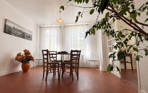 Ein Essbereich mit Tisch und Stühlen, einem Blumentopf und einem Fenster mit Vorhängen.