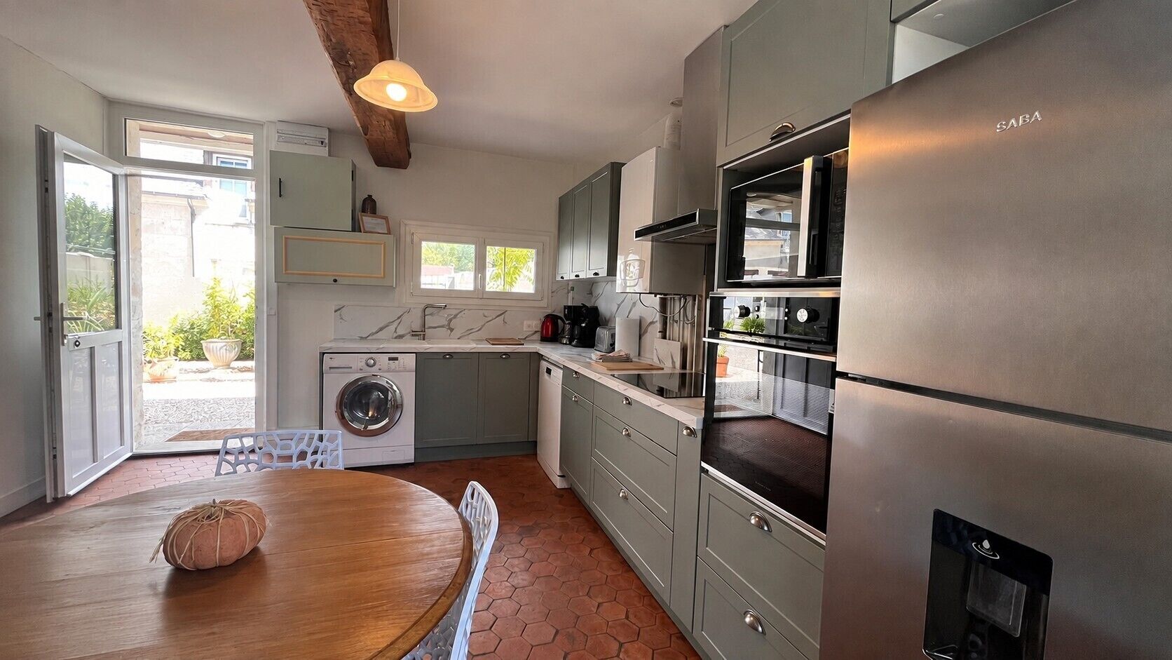 Een moderne keuken met een ingebouwde wasmachine, een eethoek met een houten tafel en uitzicht buiten via een glazen deur.