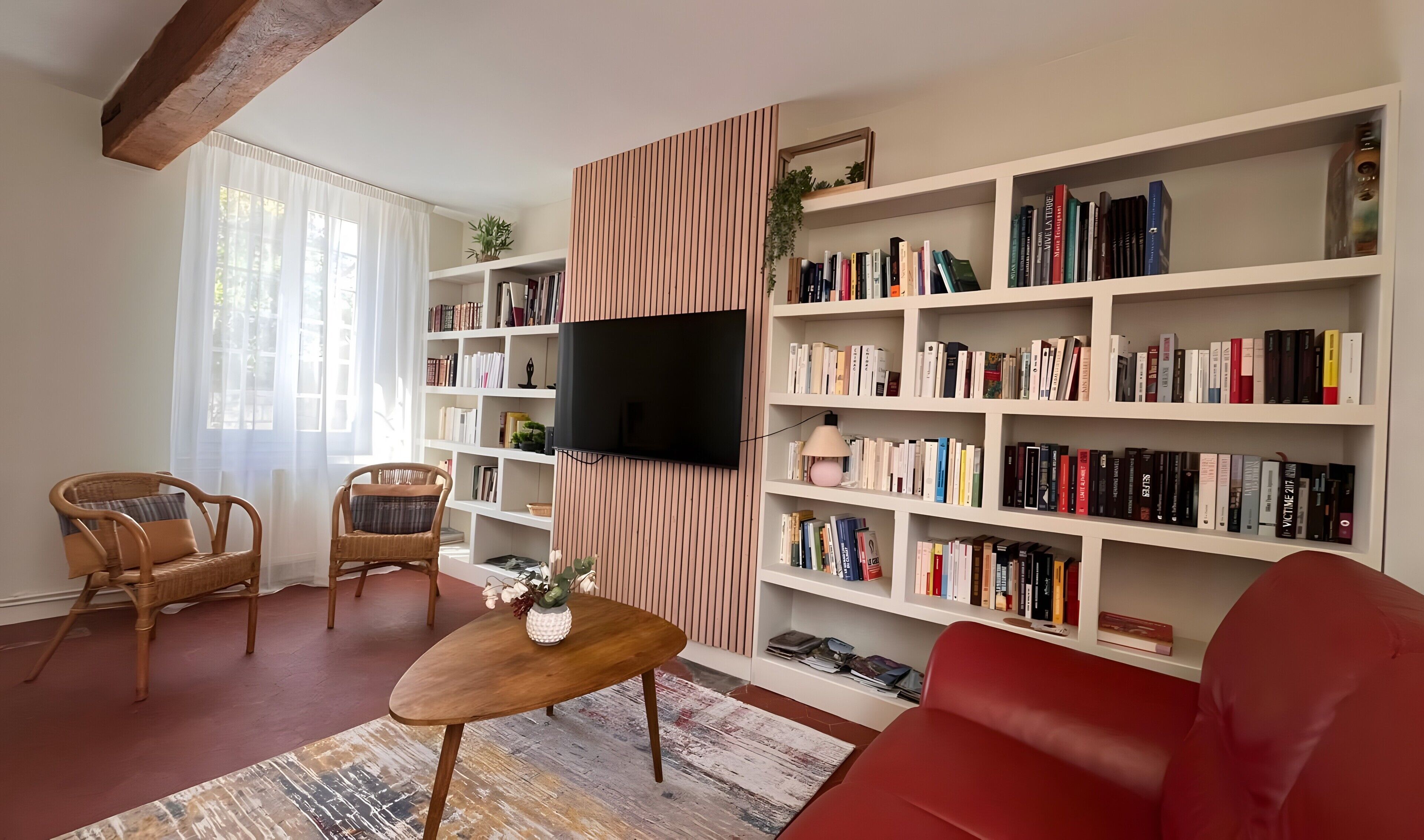Een woonkamer met een rode bank, een houten salontafel, een boekenkast en een flatscreen televisie aan de muur.