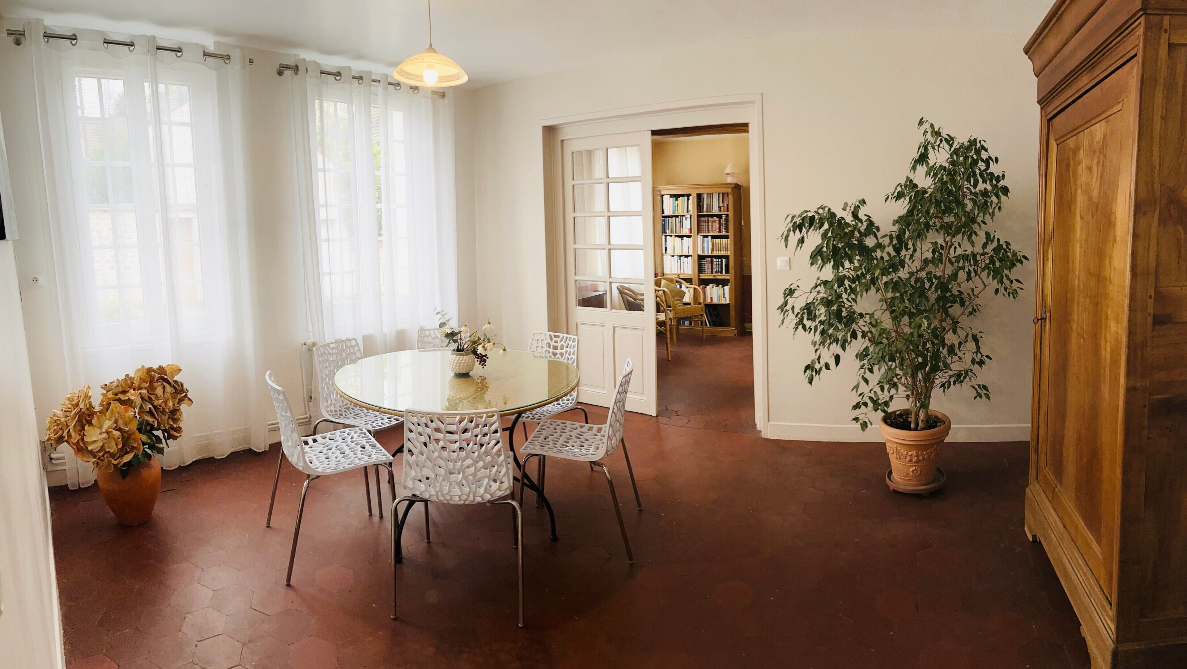 Uma sala de jantar com uma mesa redonda e cadeiras, um vaso de planta e um armário de madeira.