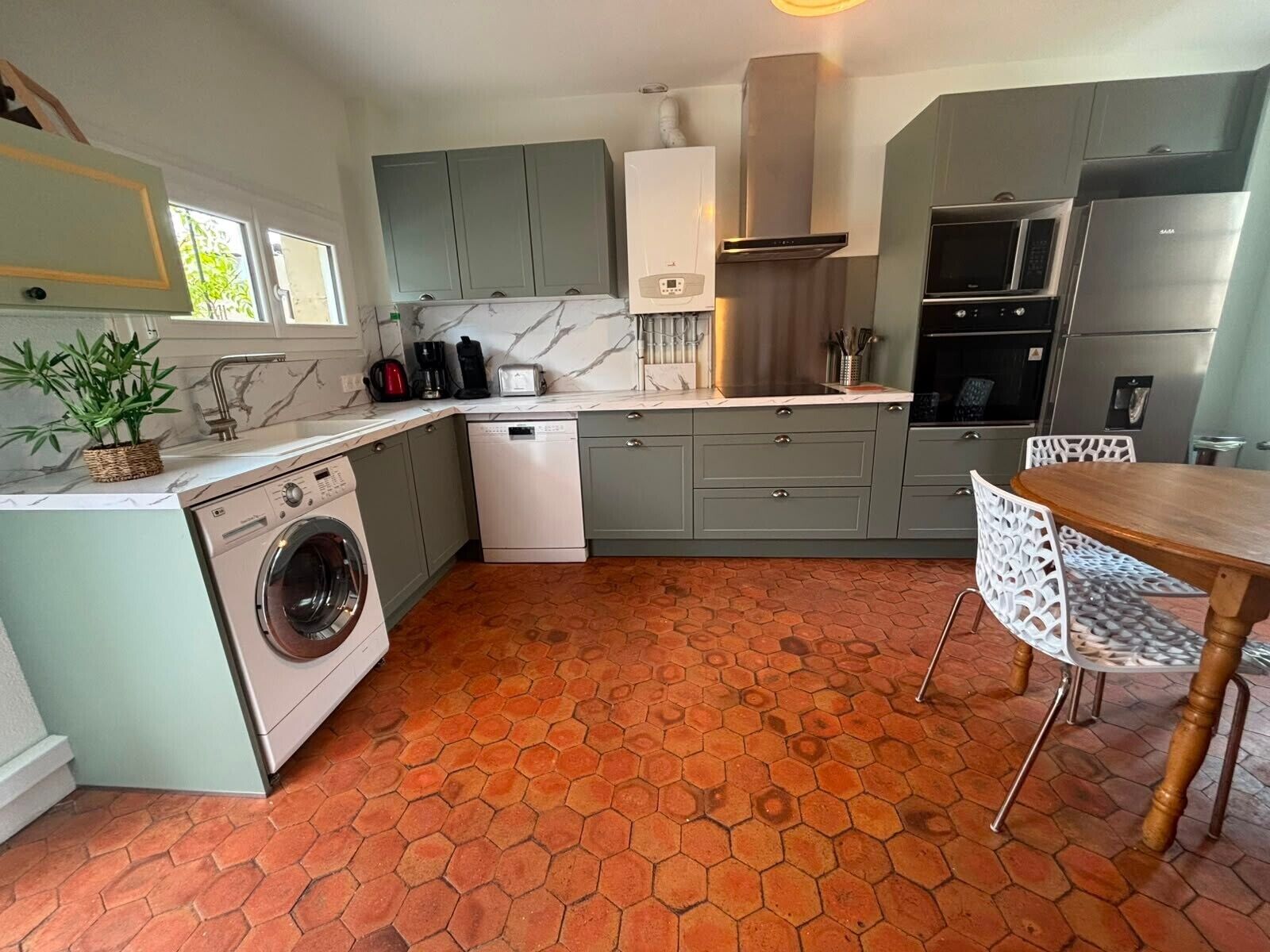 Une cuisine compacte équipée d’un lave-linge, d’un lave-vaisselle et d’un coin repas avec une table et des chaises.