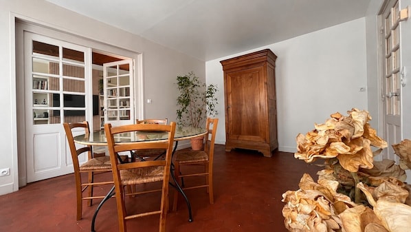 A dining area with a glass-top table, wooden chairs, a cabinet, and a potted plant.