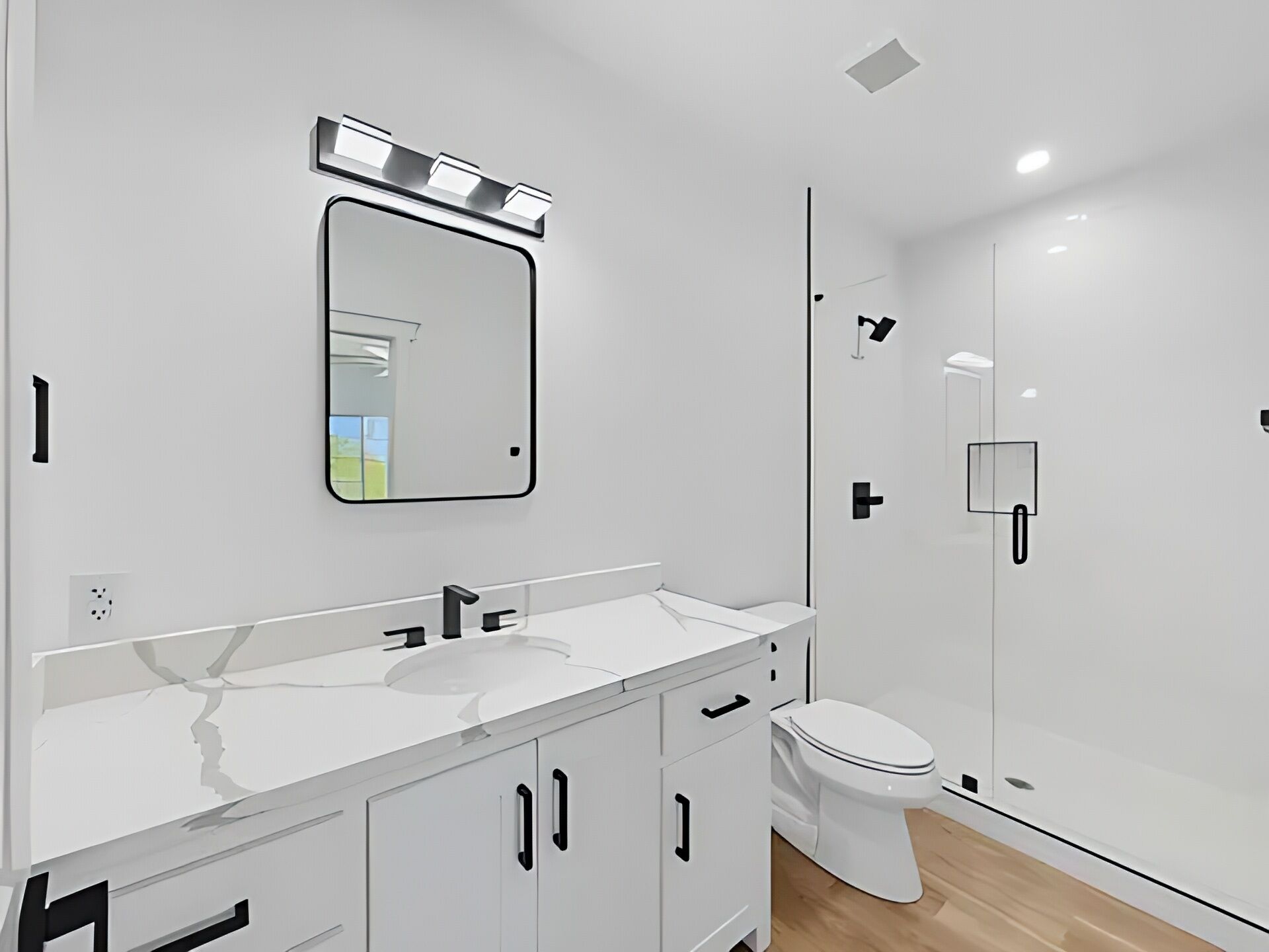 Un bany modern amb un lavabo blanc, un mirall, un vàter i una zona de dutxa.