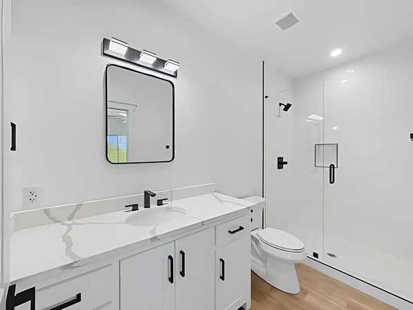 A modern bathroom with a white vanity, a mirror, a toilet, and a shower area. - Rocker B is only a 10 minute drive away from this cute lake front cabin (Graford)