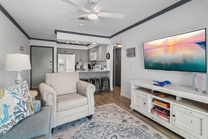 Ein Wohnzimmer mit einer Couch, einem Fernseher und einer Küche im Hintergrund.