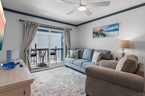 Ein Zimmer mit einer Couch, einem Sessel, einem Tisch, einer Lampe, einem Gemälde und einem Deckenventilator.