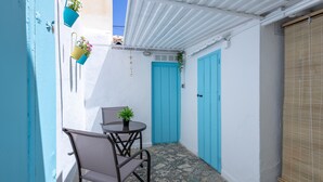 Uno spazio esterno stretto con un tavolo, sedie, una porta blu e piante in vaso.