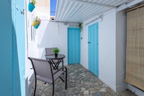 Ein schmaler Außenbereich mit Tisch und Stühlen, einer blauen Tür und Kübelpflanzen.