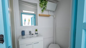 Un bagno con lavandino, specchio e water bianchi. In parete, piante in vaso e un telaio di porta blu.
