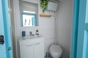 Ein Badezimmer mit einem weißen Waschbecken, Spiegel und Toilette. An der Wand stehen Topfpflanzen und der Türrahmen ist blau.