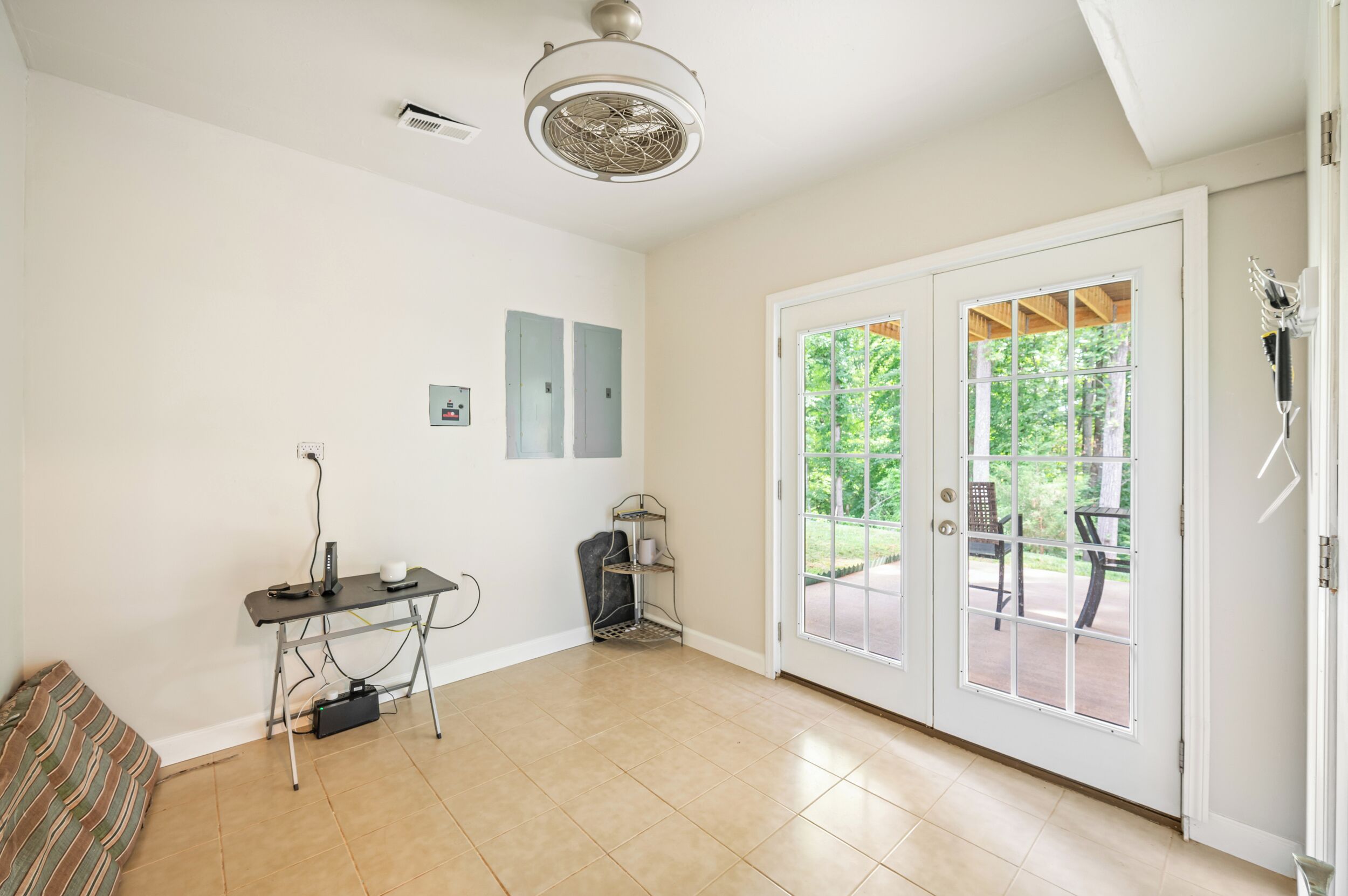 Une pièce spacieuse dotée d’une grande porte-fenêtre coulissante donnant sur un patio extérieur, d’un ventilateur de plafond et d’une multiprise au sol.