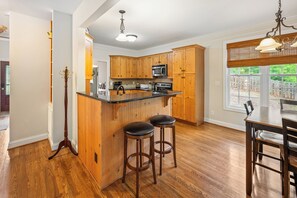 Een keuken met houten kastjes, een centraal eiland met krukken, een eettafel met stoelen, en een uitzicht door een raam.