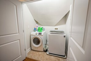 A laundry room with a washing machine, dryer, and cleaning supplies. - Boonsboro Escape (Lynchburg)