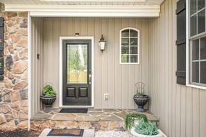 A house entrance with a stone wall, a black door, and two potted plants on either side. - Boonsboro Escape (Lynchburg)