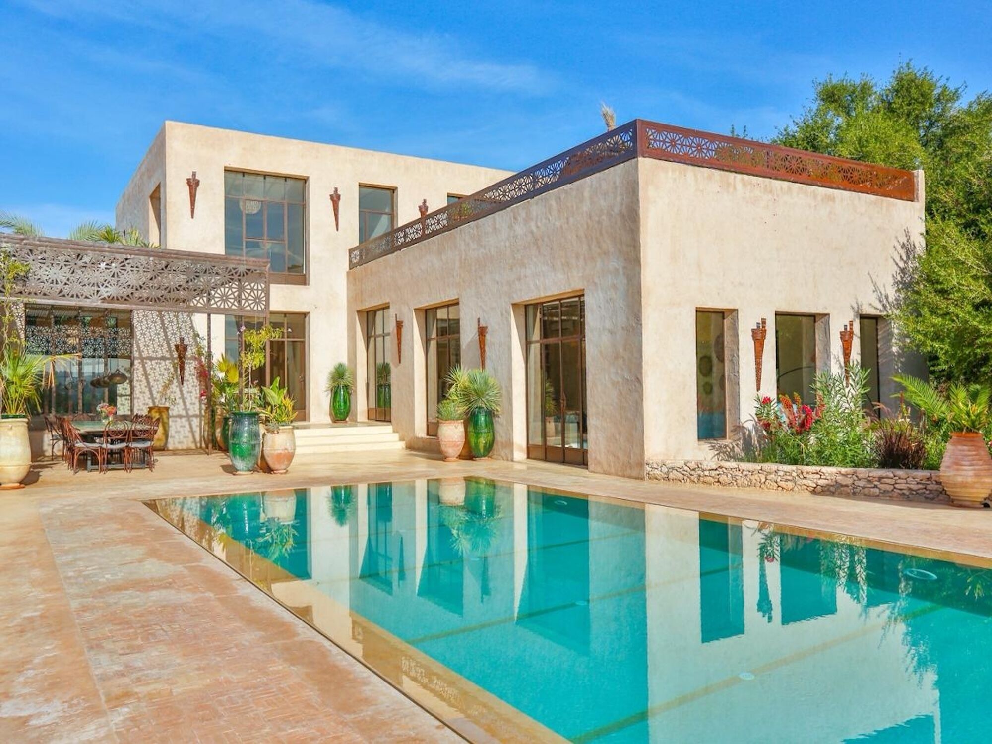 Une maison moderne à deux étages, dotée d’une piscine, de mobilier d’extérieur et de plantes en pot.