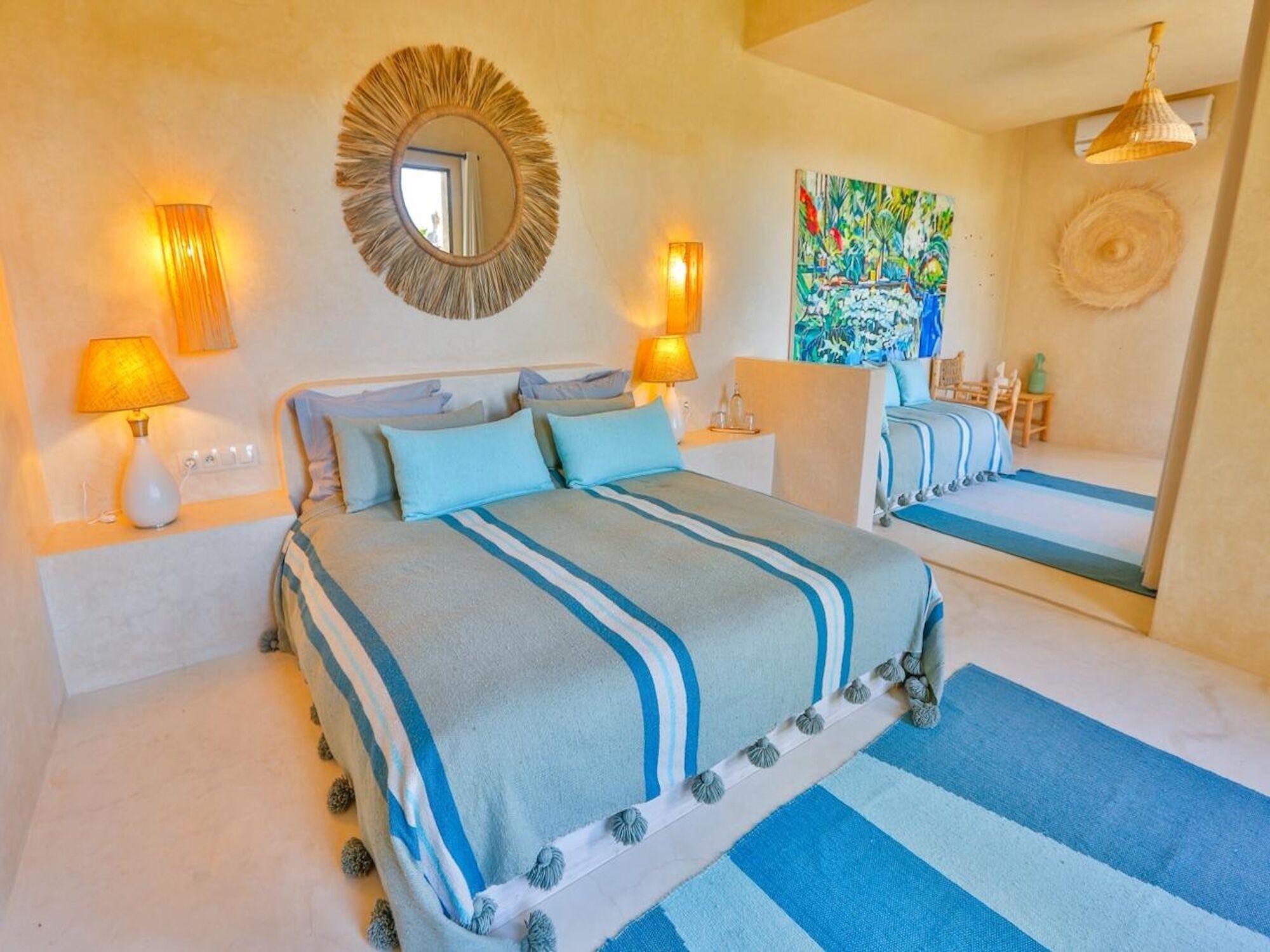 A hotel room with a bed, two bedside lamps, a mirror, a painting, and a window.