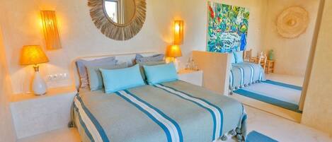A hotel room with a bed, two bedside lamps, a mirror, a painting, and a window.