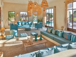 A spacious living area with a large sofa set, a coffee table, and a view of a pool through large windows. - Palais Baraya (Essaouira)