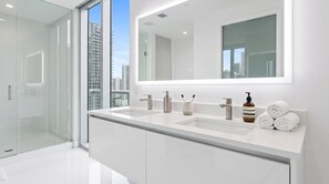 A modern bathroom with a large mirror, two sinks, and a glass shower enclosure. - Luxury suite with city and bay views in Miami (Miami)