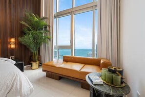 A modern hotel room with a large window, a sofa, a bed, a potted plant, and a small table with decorative items. - Luxury suite with city and bay views in Miami (Miami)