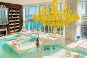 A spacious indoor swimming pool with a large window view of the city, a grand chandelier, and a library with bookshelves. - Luxury suite with city and bay views in Miami (Miami)