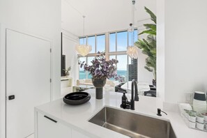 A modern kitchen with a large window, a white countertop, a sink, and a vase with flowers. - Luxury suite with city and bay views in Miami (Miami)