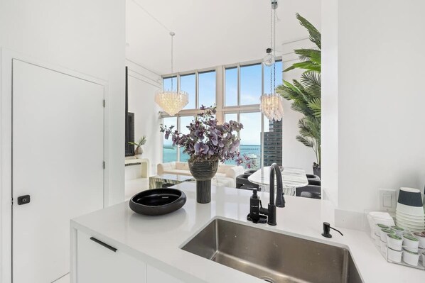 A modern kitchen with a large window, a white countertop, a sink, and a vase with flowers. - Luxury suite with city and bay views in Miami (Miami)