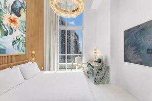 A hotel room with a large bed, a desk with a marble top, a large window with a view of buildings, and a painting on the wall. - Luxury suite with city and bay views in Miami (Miami)