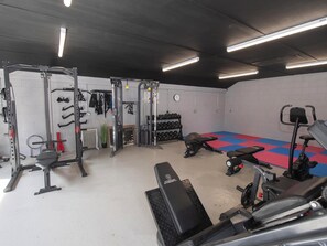 Ein Fitnessstudio mit verschiedenen Trainingsgeräten, darunter eine Langhantelbank, Kurzhanteln und ein Squat-Gestell.