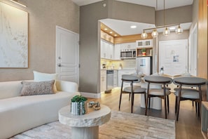 Een moderne woonkamer met een bank, een bijzettafeltje met decoratieve objecten, en uitzicht op de keuken met een eethoek.