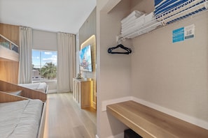 A hotel room with a bed, a desk, a hanging clothes rack, and a window with a view of palm trees. - 1BR apartment with 2 queens near Disney (Orlando)