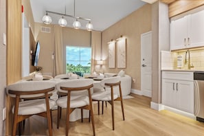 A modern kitchen with white cabinets, a stainless steel dishwasher, and a window overlooking greenery. - 1BR apartment with 2 queens near Disney (Orlando)