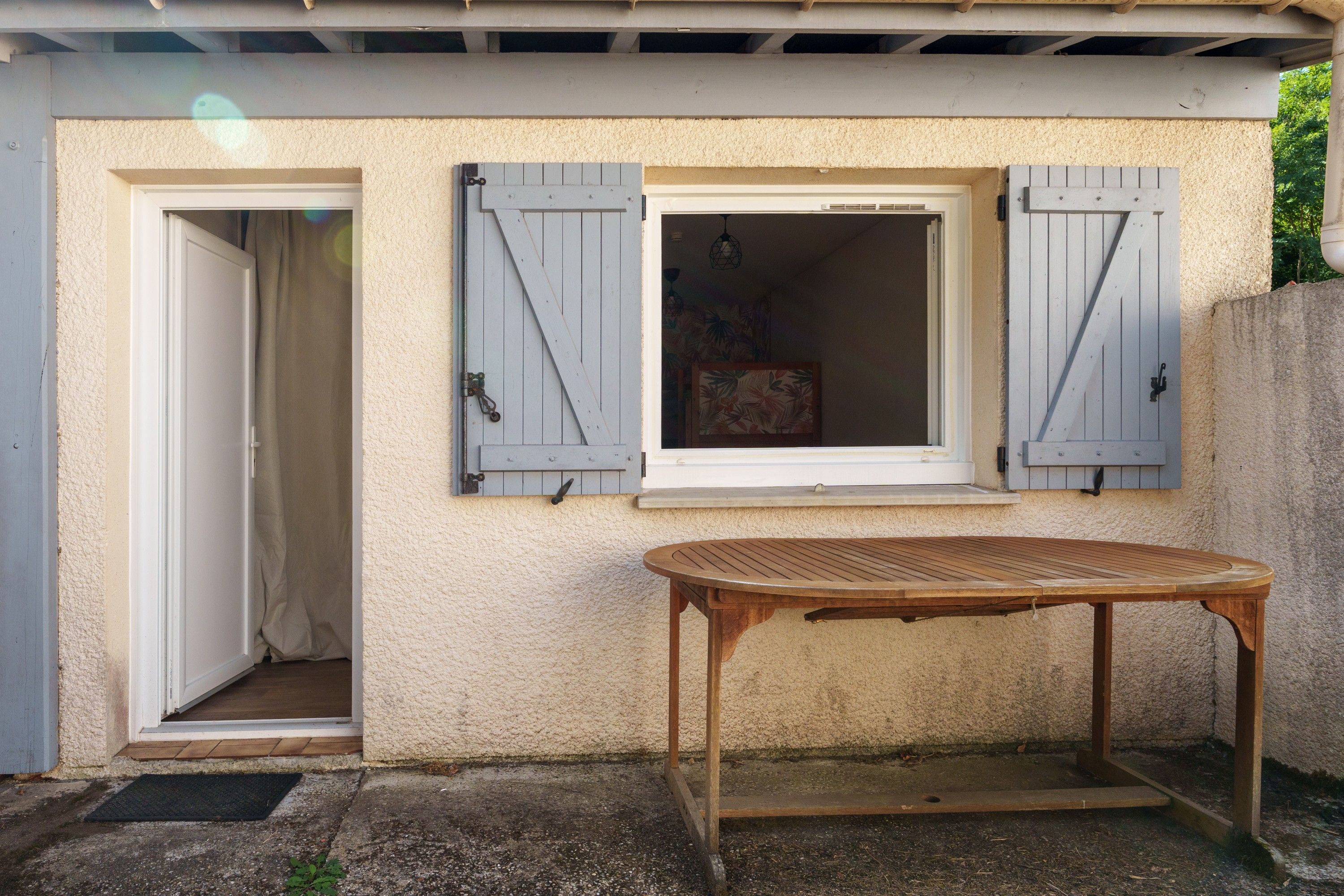 A building with a door and a window, a wooden table in front, and a textured wall.