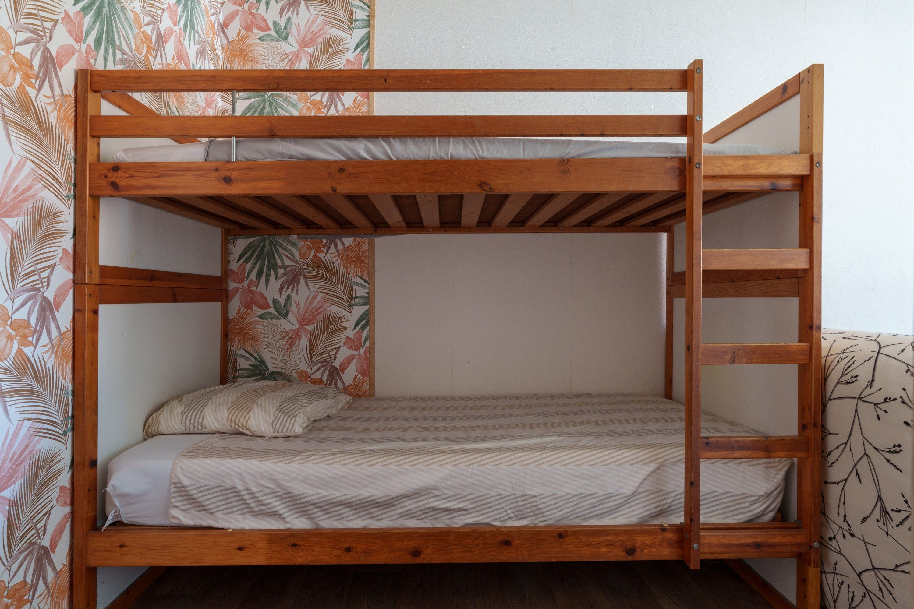 Een stapelbed met een houten frame, een matras met gestreept beddengoed en een kussen.