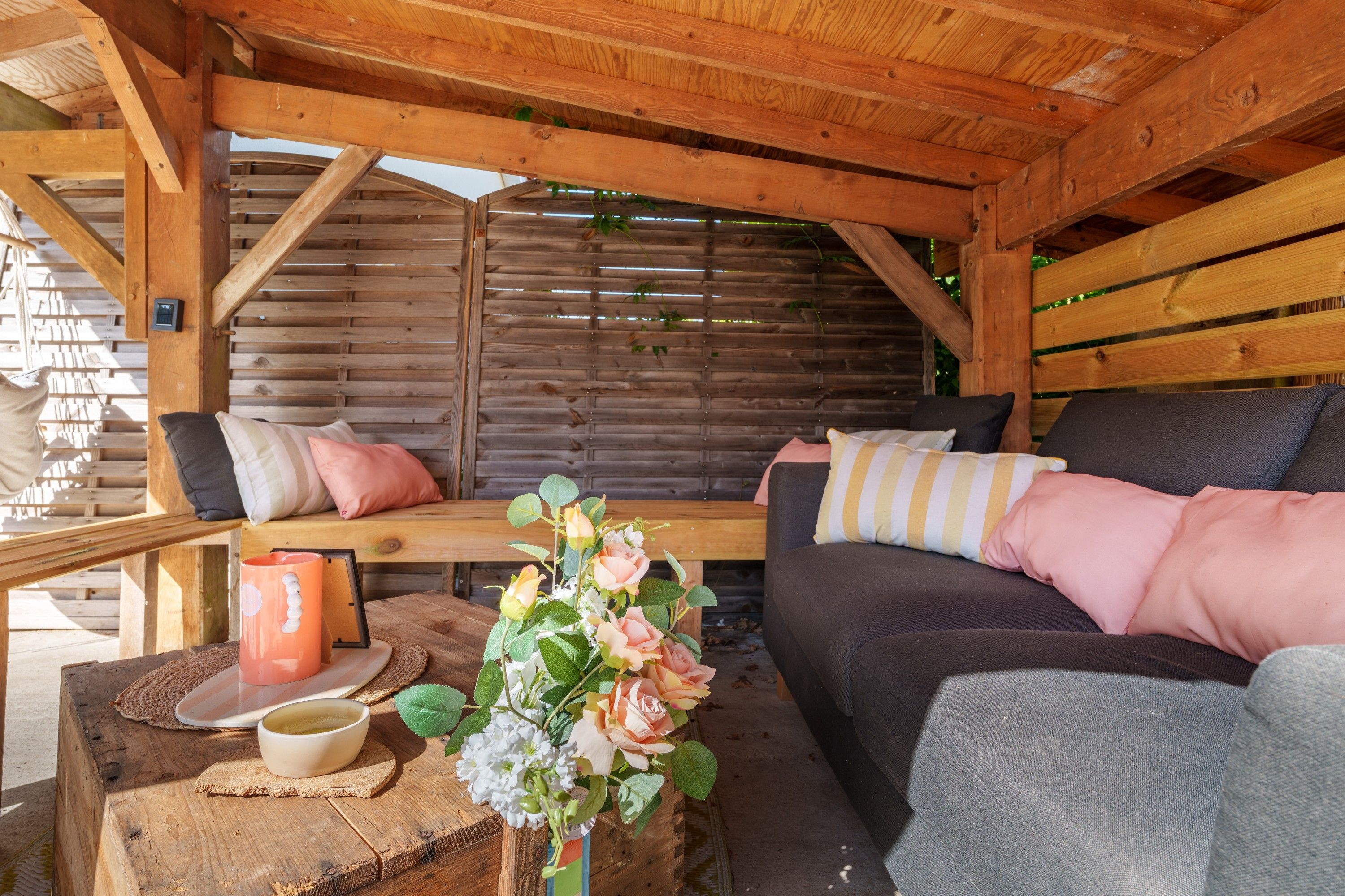 Een houten chaletinterieur met een bank, kussens, een tafel met een mok en een bloemstuk.