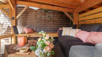 Een houten chaletinterieur met een bank, kussens, een tafel met een mok en een bloemstuk.