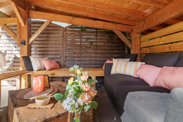 A wooden cabin interior with a sofa, cushions, a table with a mug and a flower arrangement.
