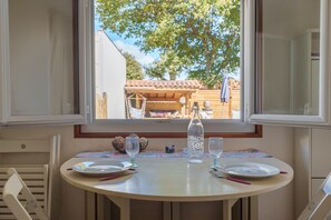 A dining table with plates, a bottle, and glasses, set against a window overlooking a garden.