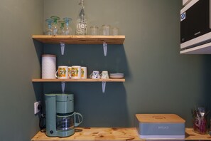 A kitchen with wooden shelves holding glassware, mugs, and a coffee maker.