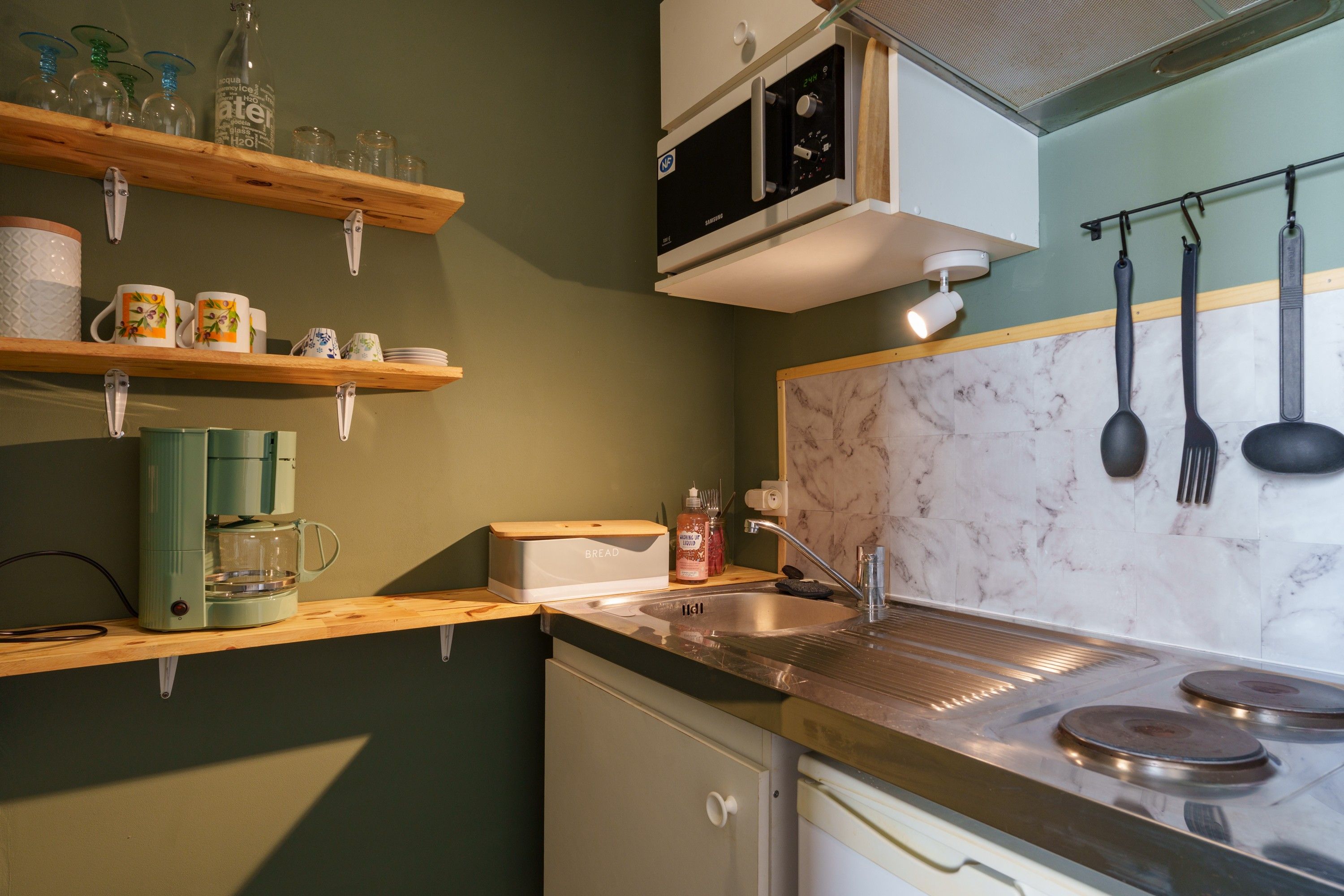 A kitchen with a built-in microwave, a sink, and a stove. There are shelves above the counter holding glassware and a coffee maker.