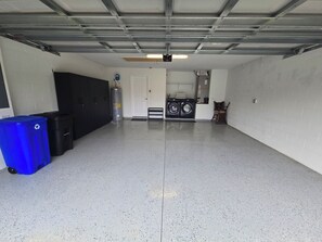 A garage with a washing machine, two trash bins, a water heater, and a ceiling fan.