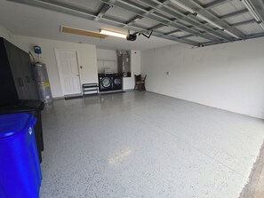 A spacious garage with a washing machine, a chair, and a blue trash bin. - Terrific Pool Home, close to Flagler Beach & Daytona (Palm Coast)