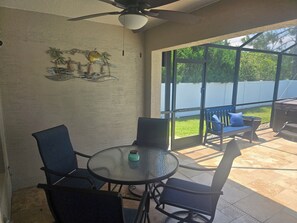 A covered patio with a round table and chairs, a ceiling fan, and a view of a backyard with a white fence. - Terrific Pool Home, close to Flagler Beach & Daytona (Palm Coast)