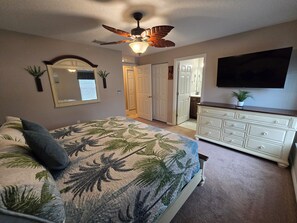 A bedroom with a bed, a dresser, a ceiling fan, a mirror, and a television.