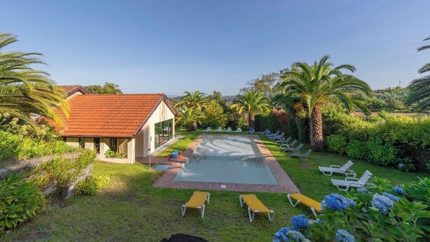 A poolside area with lounge chairs, a small building, and lush greenery.