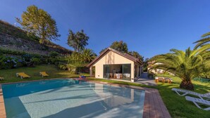 A swimming pool with lounge chairs, a covered patio, and a stone retaining wall.