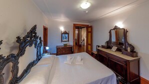 A hotel room with a large bed, a dresser with a mirror, and a door leading to another room.