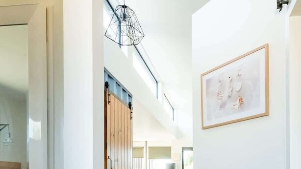 Een hal met houten vloeren, een ingelijst schilderij aan de muur, en zicht op een woonkamer met een bank en een lamp.