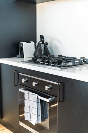 A modern kitchen with a gas stove, oven, and a towel hanging from the oven handle. - Villa Callista - Modern Coastal Escape (Port Sorell)