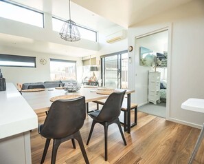 A modern kitchen with a dining area, wooden flooring, and a pendant light. - Villa Callista - Modern Coastal Escape (Port Sorell)